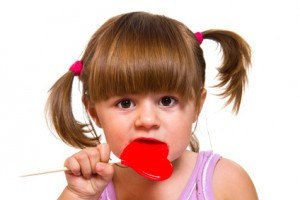 little girl eating red heart lollipop