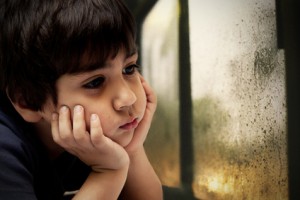 bambino che guarda la pioggia che cade dal vetro